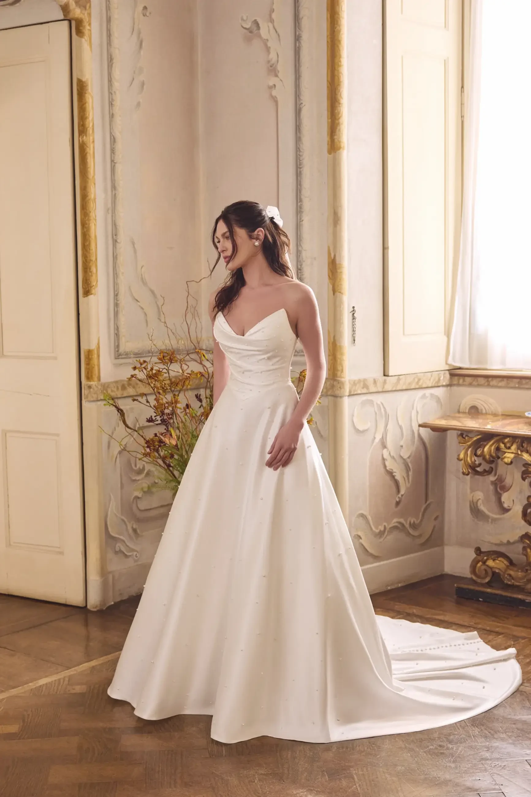 A woman in a white wedding dress stands gracefully in an elegantly decorated room.