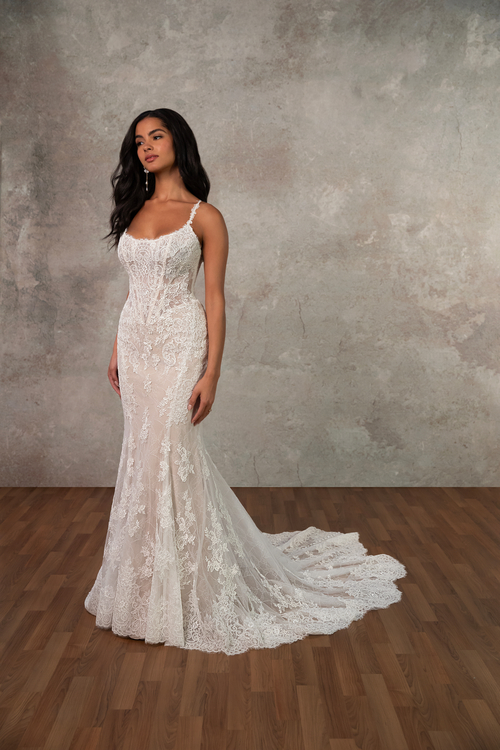 A woman in an elegant lace wedding dress stands on a wooden floor. The dress features delicate embroidery and a long, flowing train, creating a romantic atmosphere.