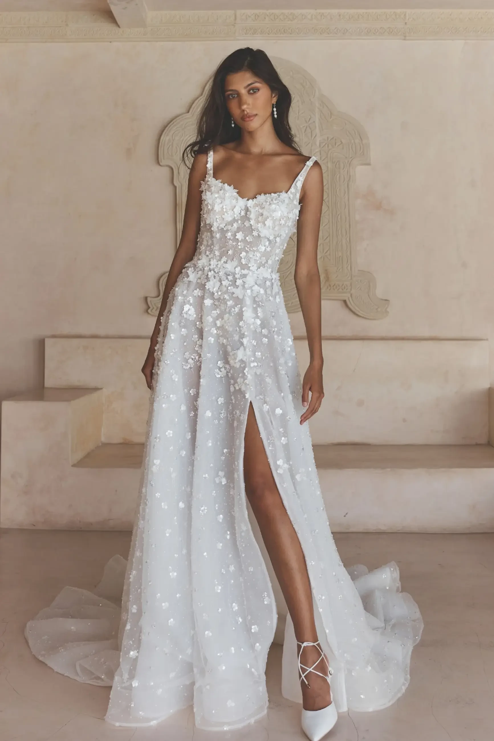 Model is wearing an a-line wedding dress with straps and 3d motifs