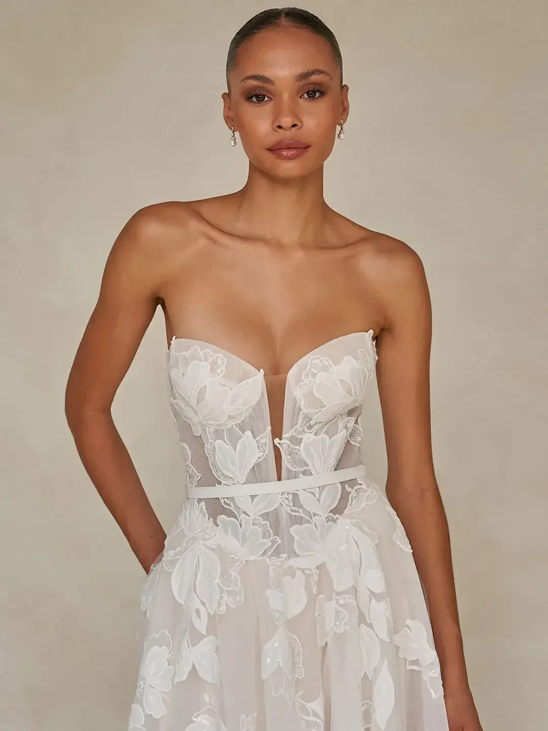 A model wearing a strapless, floral wedding dress with a deep V neckline, standing against a neutral background.