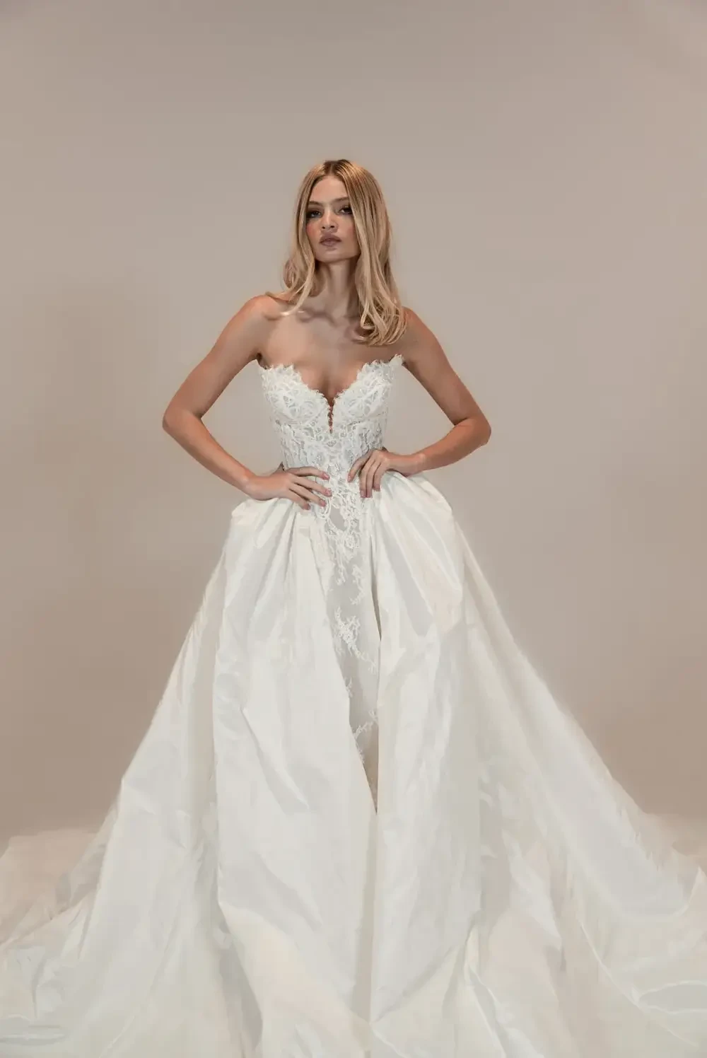 A model wearing a strapless wedding dress with intricate lace detailing and a flowing train.